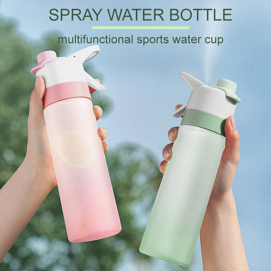 Two spray water bottles, one pink and one green, held by hands with a blurred natural background.